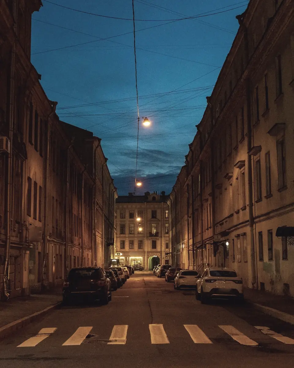 A quiet city street at dusk, with lamps and a few windows lit.